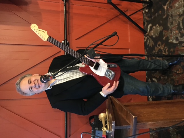Vinny smiling while playing guitar and singing into a microphone